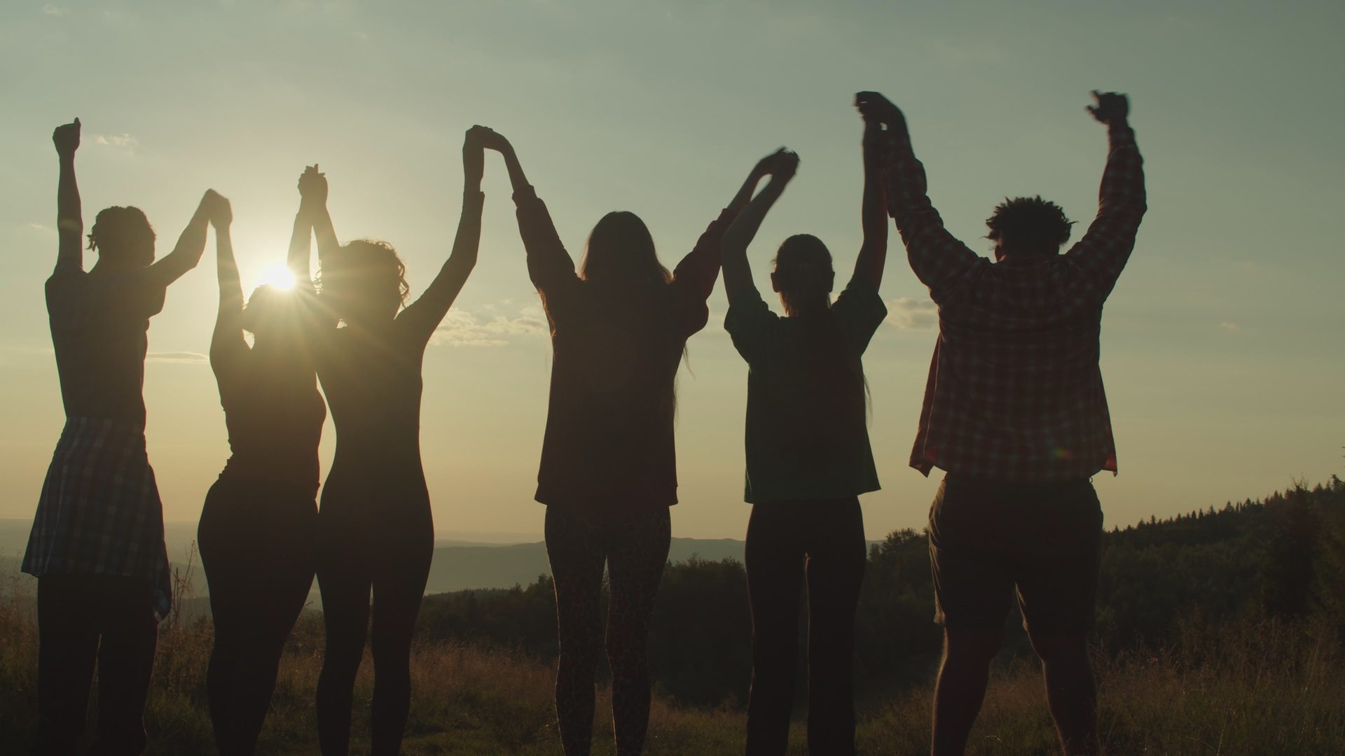Silhouettes of excited friends standing with their arms raised in celebration